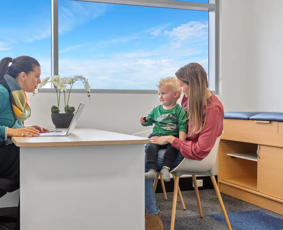A Paeds Plus clinician talking with a mother and her young son in a bright consulting room